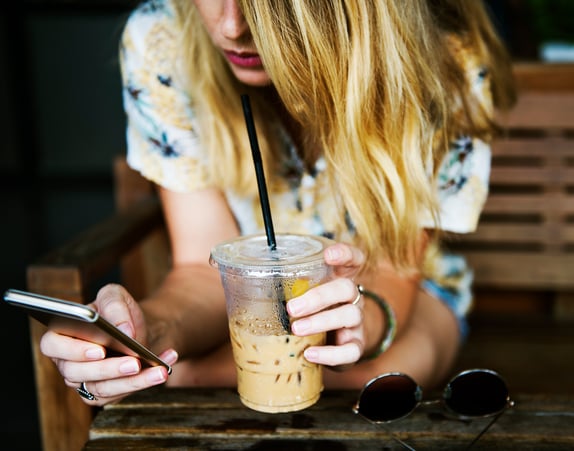 Woman drinking iced coffee and looking at her phone, representing mobile qual